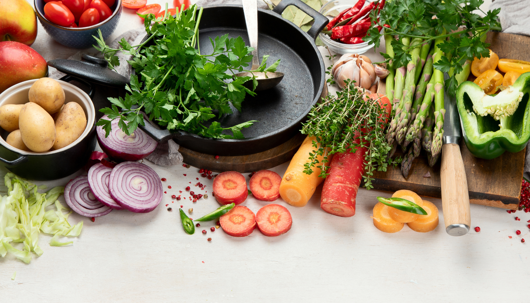 Different Vegetables Including Onion, Tomato Potato and Green Veg along with a Cooker and Cutting Board